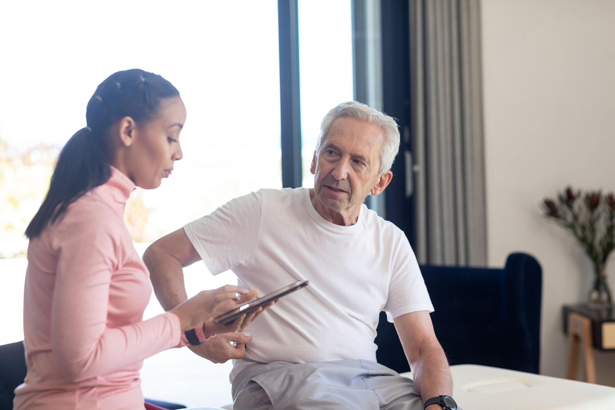 Biracial female physiotherapist with digital tablet discussing with caucasian senior man Shockwave Therapy