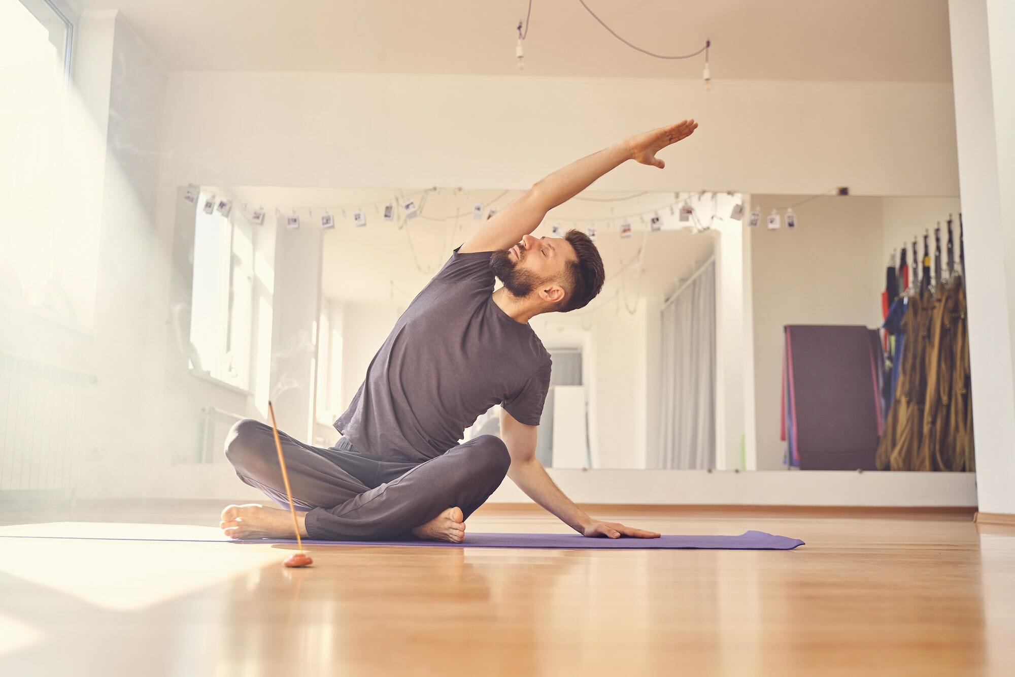 Handsome young man doing stretching exercise in yoga studio